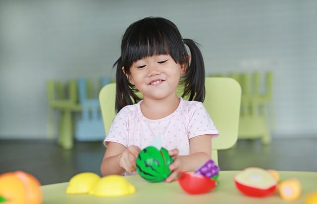 Une fille en train de jouer avec un jeu d'imitation - dinette fruits à découper